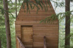 Outlandia Field Station, Glencoe. Wooden cabin amongst the treetops with trapezoidal roof. View with walkway