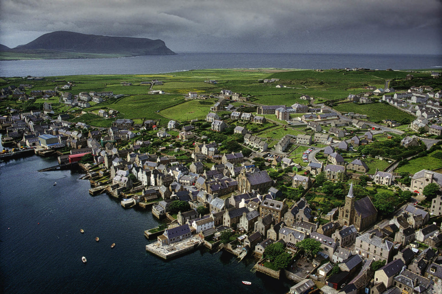 Stromness, Orkney from the air, by Richardson. Piers just into the sea and behind the town a view to the island of Hoy