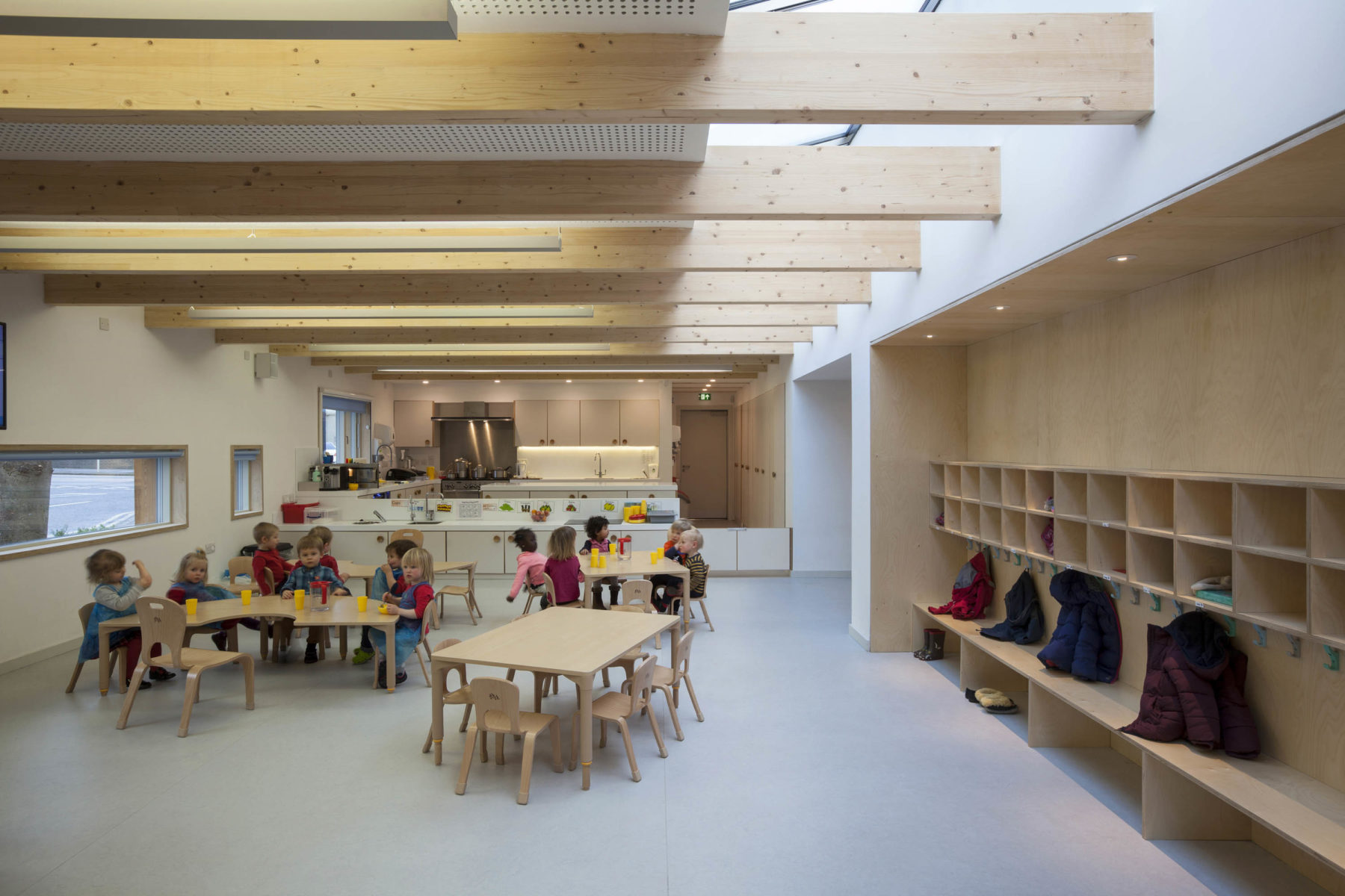 Arcadia Nursery, University of Edinburgh. Interior view showing timber beams, shelving. Children seated at tables.Malcolm Fraser Architects Arcadia Nursery Photograph by Angus Bremner